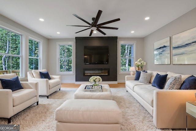 living room featuring light hardwood / wood-style floors, a healthy amount of sunlight, ceiling fan, and a large fireplace