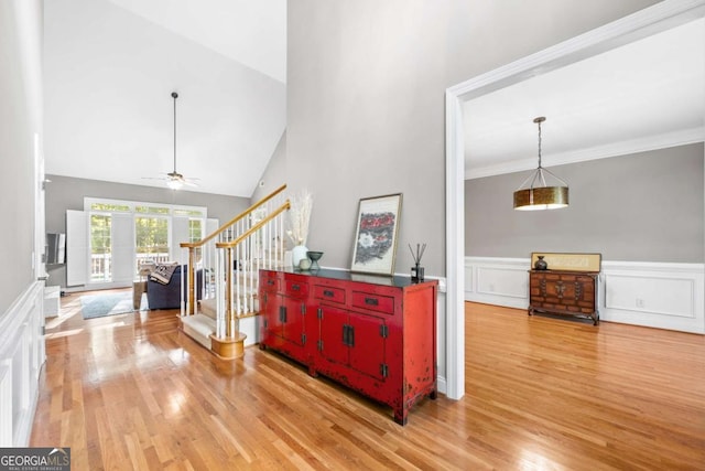 corridor with ornamental molding, a wainscoted wall, light wood-style flooring, and stairs