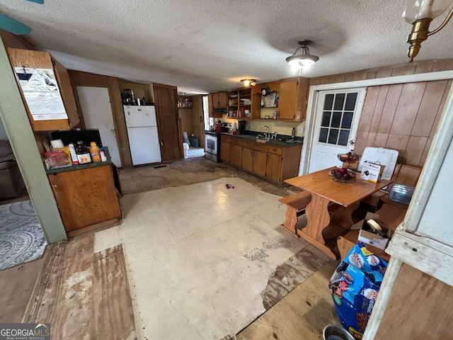 kitchen featuring electric range, white refrigerator, wooden walls, and a textured ceiling