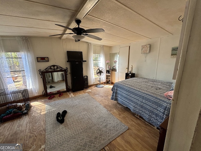 bedroom featuring multiple windows, vaulted ceiling with beams, ceiling fan, and wood-type flooring