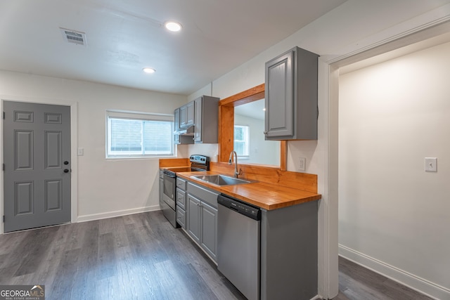 kitchen with sink, butcher block counters, gray cabinetry, dark hardwood / wood-style floors, and stainless steel appliances