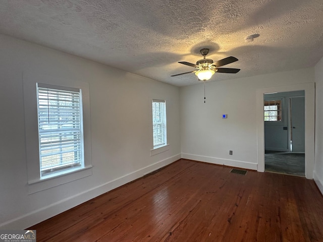 spare room featuring dark wood-style floors, visible vents, a ceiling fan, a textured ceiling, and baseboards