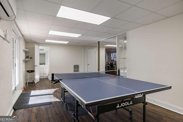 recreation room featuring a drop ceiling, dark wood-type flooring, and a wall mounted air conditioner