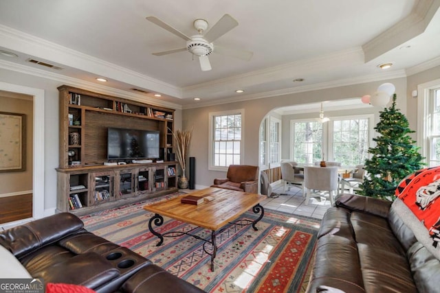 tiled living room with a tray ceiling, crown molding, and ceiling fan