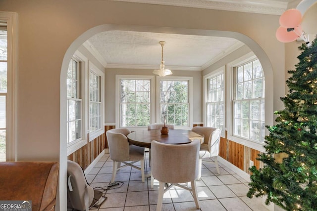 dining room with crown molding, wood walls, and light tile patterned floors