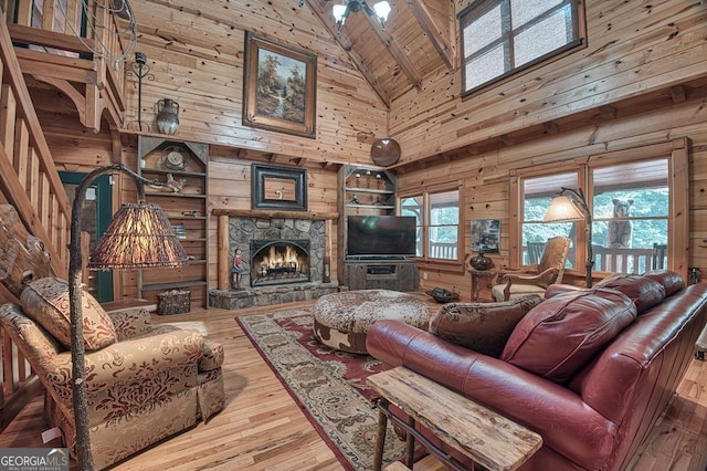 living room featuring high vaulted ceiling, wood walls, a stone fireplace, and wood finished floors