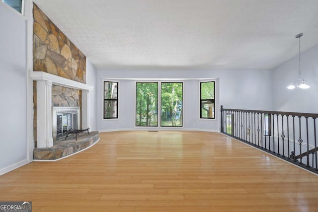 unfurnished living room featuring light wood-type flooring, a textured ceiling, a chandelier, and a fireplace