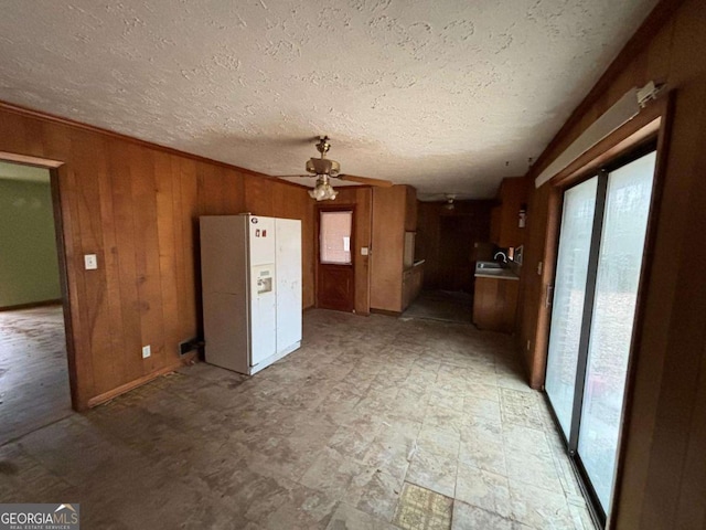 unfurnished living room featuring ceiling fan, sink, wood walls, and a textured ceiling