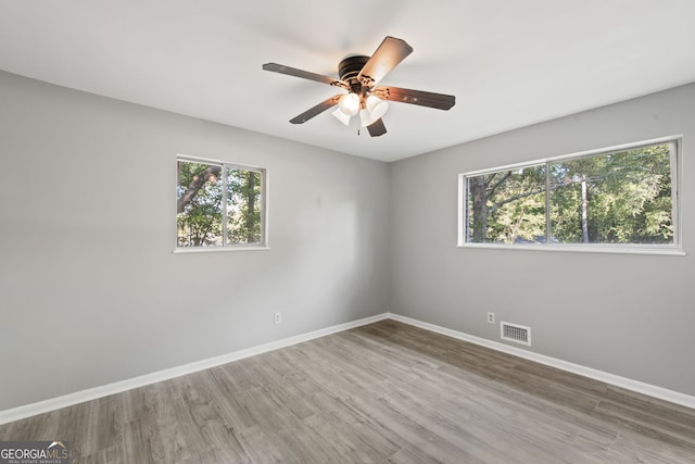 unfurnished room with a wealth of natural light, wood finished floors, visible vents, and baseboards