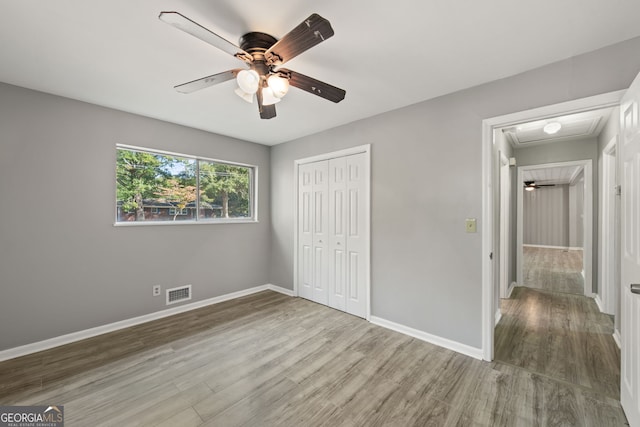 unfurnished bedroom featuring a closet, visible vents, a ceiling fan, wood finished floors, and baseboards