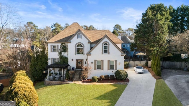 view of front facade featuring a chimney, stucco siding, fence, driveway, and a front lawn