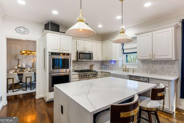 kitchen featuring white cabinets, appliances with stainless steel finishes, light stone counters, decorative light fixtures, and a sink