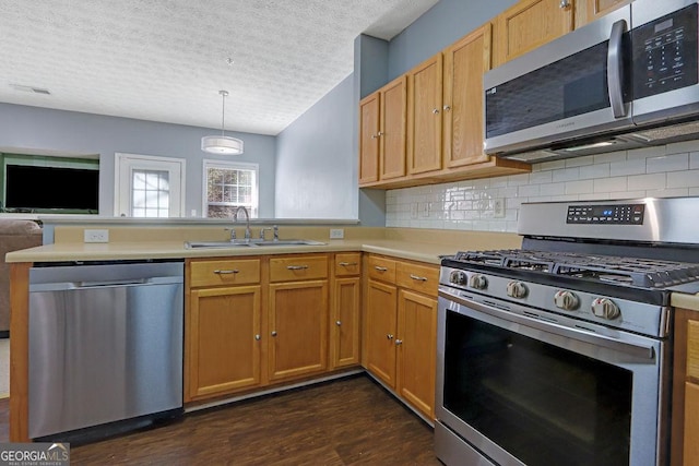 kitchen featuring dark wood-type flooring, a sink, appliances with stainless steel finishes, a peninsula, and light countertops