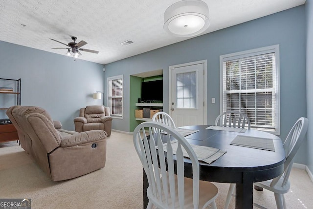 carpeted dining room with visible vents, a textured ceiling, a healthy amount of sunlight, and a ceiling fan