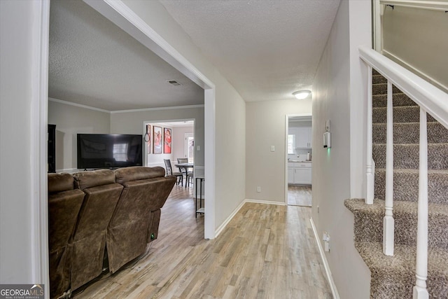 entrance foyer with a textured ceiling, ornamental molding, and light hardwood / wood-style floors