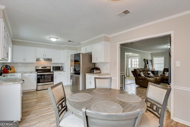 dining area with light wood-type flooring, a textured ceiling, sink, and ornamental molding