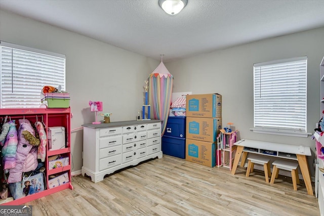 recreation room with light wood-type flooring and a textured ceiling