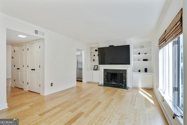 unfurnished living room with visible vents, built in features, a high end fireplace, light wood-style floors, and ornamental molding