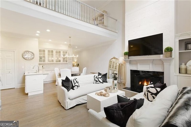 living room with light wood-type flooring, a chandelier, crown molding, and a towering ceiling