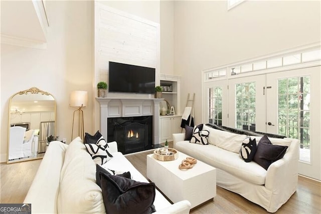 living room featuring french doors, a towering ceiling, a wealth of natural light, and light hardwood / wood-style flooring