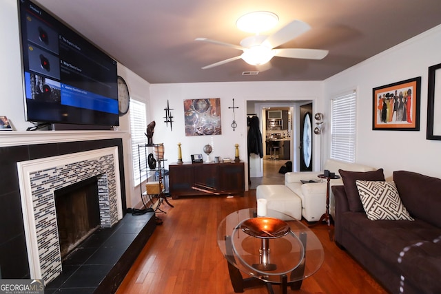 living area featuring ceiling fan, a tiled fireplace, visible vents, and wood finished floors