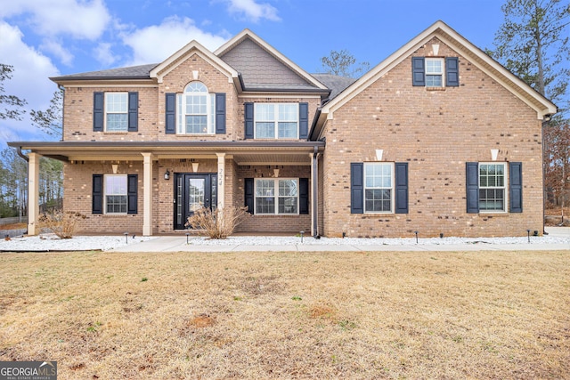 view of front of house with covered porch, brick siding, and a front lawn