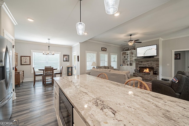 kitchen with open floor plan, light stone countertops, stainless steel appliances, a stone fireplace, and pendant lighting