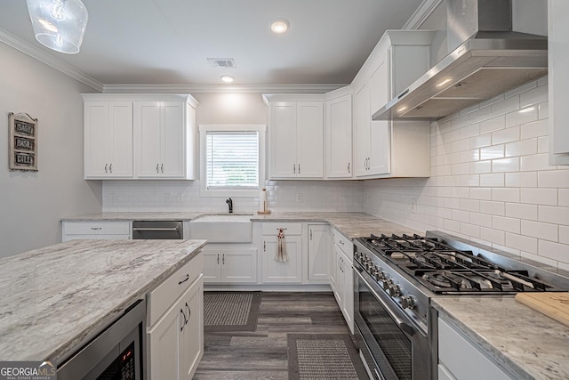 kitchen with visible vents, white cabinets, wall chimney range hood, light stone countertops, and stainless steel gas range oven