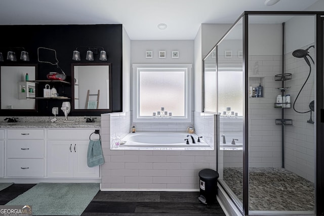 bathroom featuring a garden tub, wood finished floors, a sink, a shower stall, and double vanity