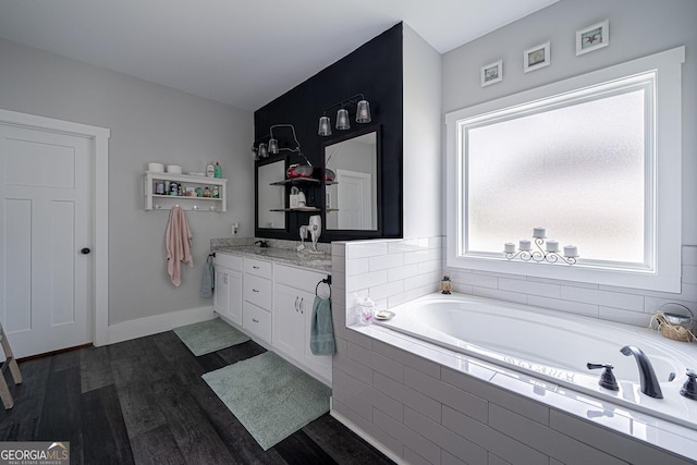 bathroom featuring double vanity, a garden tub, baseboards, and wood finished floors