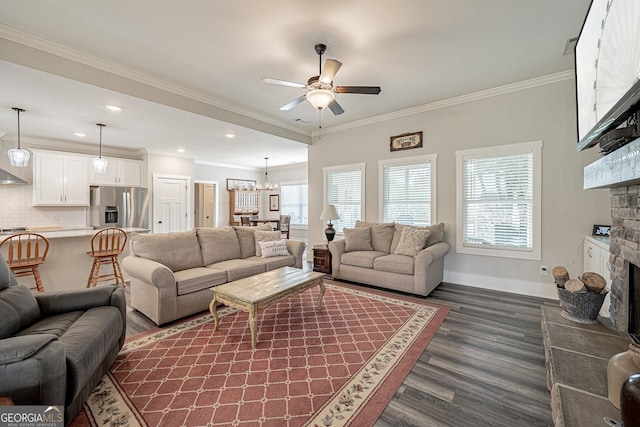 living room featuring a fireplace, ornamental molding, dark wood-type flooring, baseboards, and ceiling fan with notable chandelier