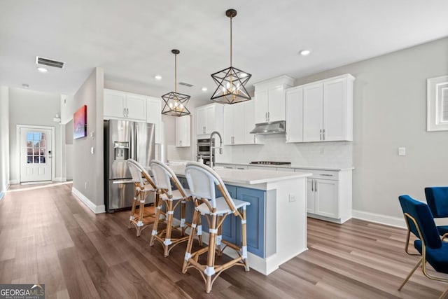 kitchen featuring a center island with sink, stainless steel appliances, light countertops, white cabinetry, and under cabinet range hood