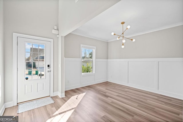 entryway featuring light wood-type flooring, an inviting chandelier, crown molding, and wainscoting