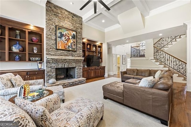 living room featuring light wood-type flooring, beam ceiling, a towering ceiling, and a fireplace