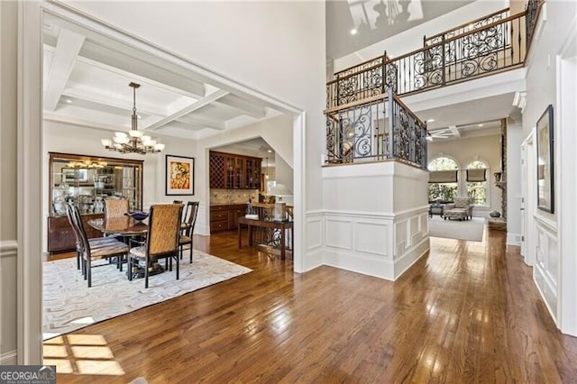 dining room with wood-type flooring, a towering ceiling, a chandelier, coffered ceiling, and beamed ceiling