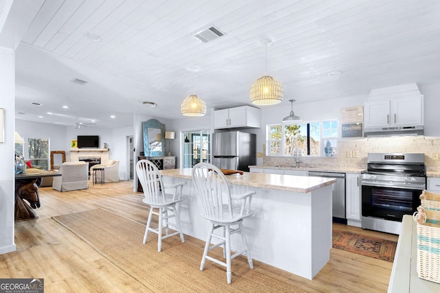 kitchen with stainless steel appliances, a sink, visible vents, decorative backsplash, and a kitchen bar