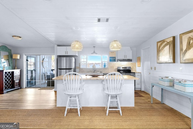 kitchen featuring stainless steel appliances, visible vents, backsplash, light wood-style flooring, and under cabinet range hood