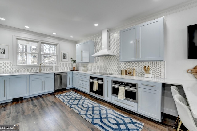 kitchen featuring stainless steel appliances, a sink, decorative backsplash, wall chimney range hood, and ornamental molding