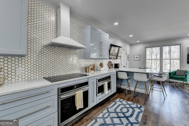 kitchen featuring a peninsula, black electric cooktop, wall chimney range hood, and oven