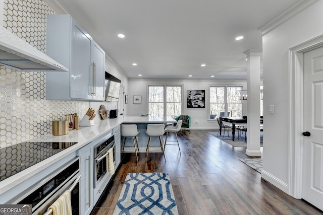 kitchen featuring wall chimney exhaust hood, oven, backsplash, and dark wood-style flooring
