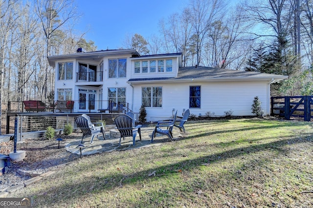 rear view of property featuring fence, a balcony, a yard, a patio, and an outdoor fire pit