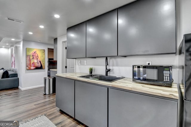 kitchen with a sink, baseboards, gray cabinetry, wood counters, and black appliances