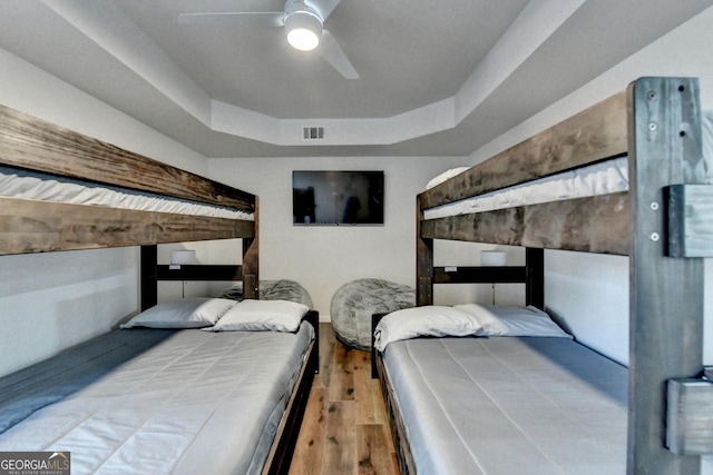 bedroom featuring a raised ceiling, wood finished floors, visible vents, and a ceiling fan