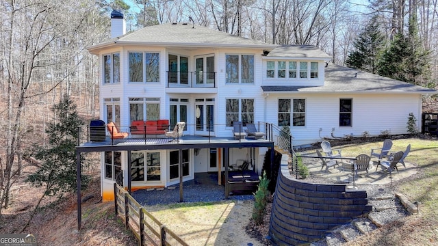 back of house featuring a chimney, a wooden deck, a patio area, a shingled roof, and an outdoor fire pit