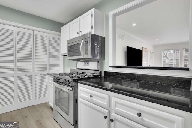 kitchen featuring white cabinets, light wood-type flooring, appliances with stainless steel finishes, and dark stone countertops