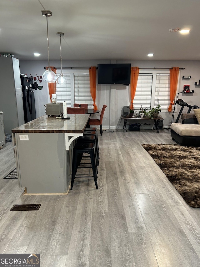 kitchen with visible vents, a kitchen breakfast bar, freestanding refrigerator, light wood finished floors, and decorative light fixtures