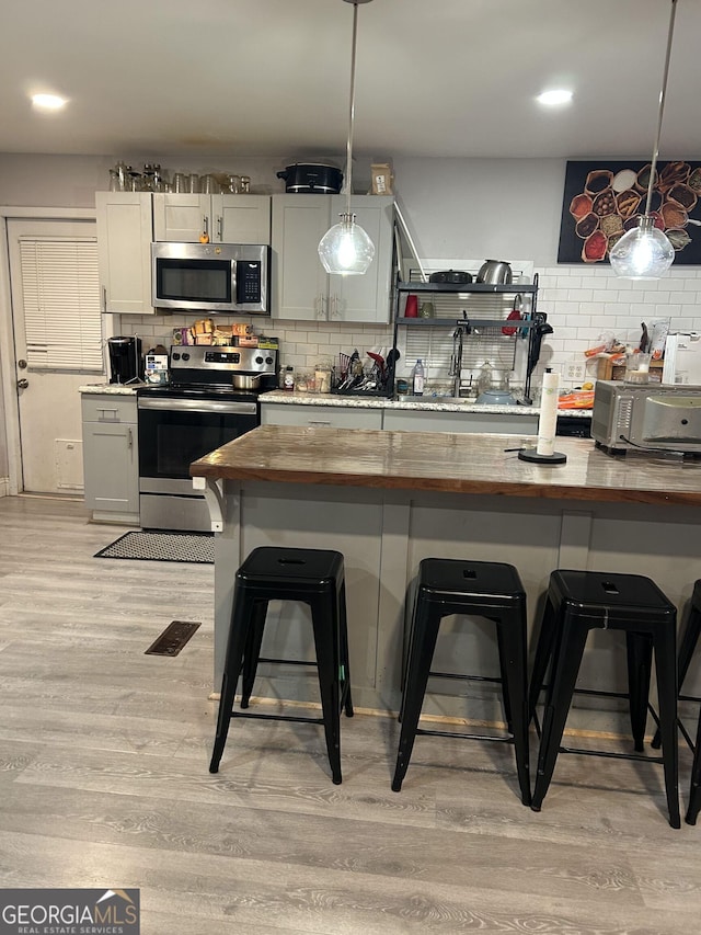 kitchen with wooden counters, stainless steel appliances, a kitchen breakfast bar, and decorative light fixtures