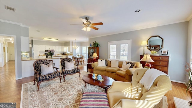 living room featuring ceiling fan with notable chandelier, light wood-type flooring, and crown molding