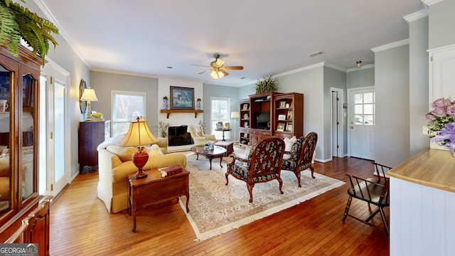 living room with ornamental molding, a brick fireplace, ceiling fan, and light hardwood / wood-style flooring