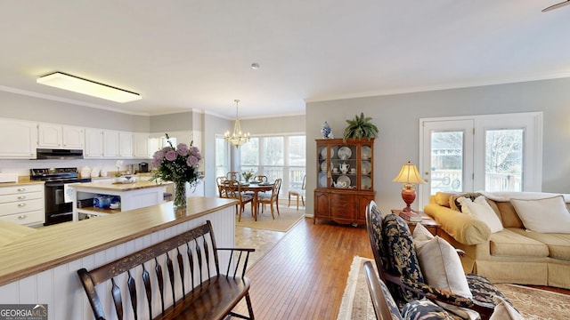 living room with ornamental molding, a notable chandelier, a wealth of natural light, and light hardwood / wood-style flooring